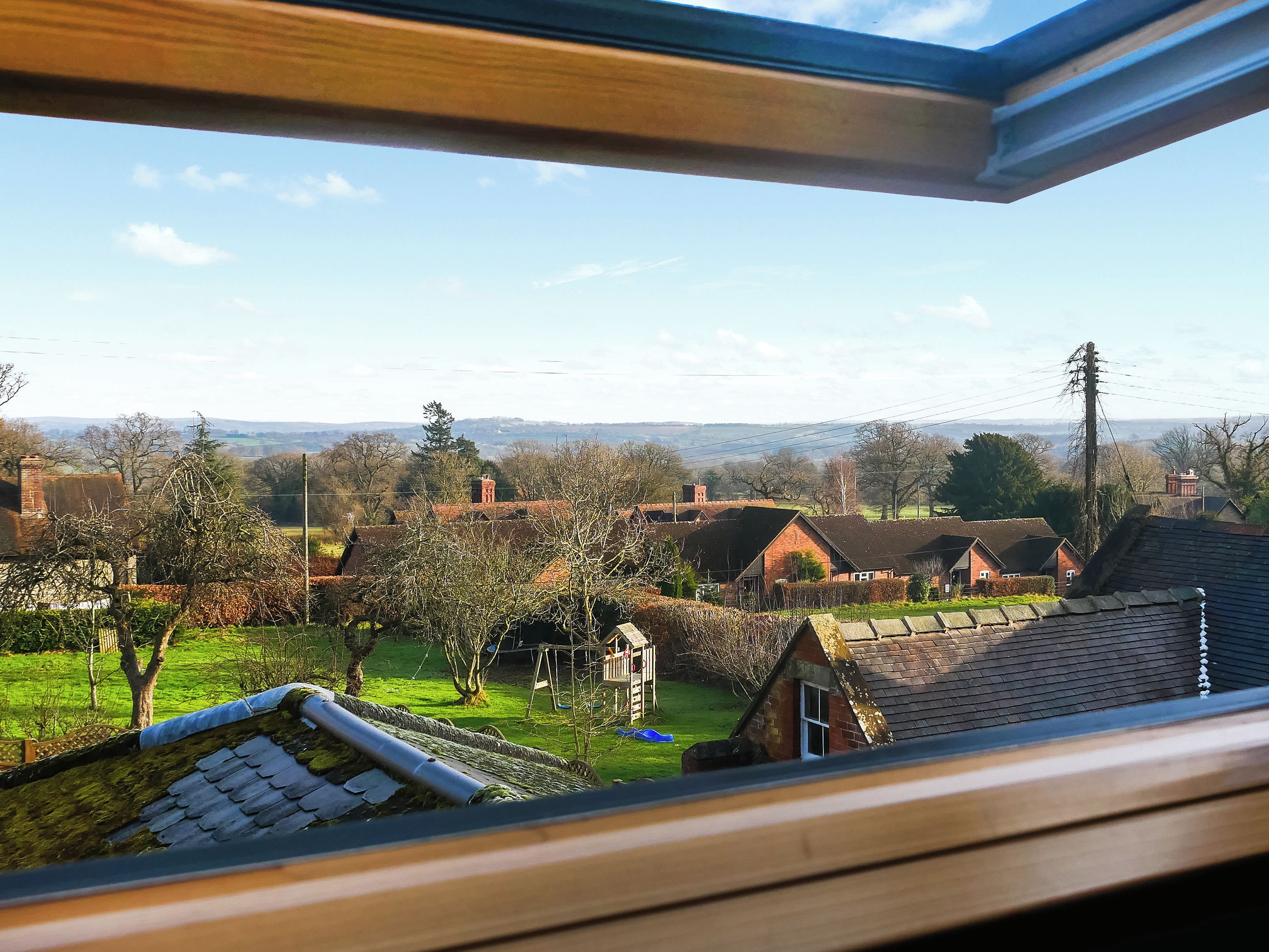 A view from a window overlooking a rural landscape with houses, trees, and a clear sky.