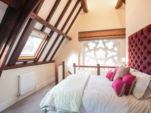 Een slaapkamer met een schuine kap, een groot raam met een decoratieve witte omlijsting, een rode, gestuifte hoofdbord en een witte radiator.