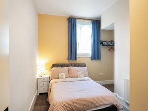 A bedroom with a bed, a nightstand, a lamp, a window with curtains, and a radiator. - The Old School House 1-UK32061 (Burwarton, near Bridgnorth)