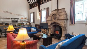 A cozy living room with a fireplace, blue sofas, a coffee table, and a kitchen area with shelves and appliances.