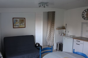 Une pièce de taille modeste comprenant un lit, une table à manger, un coin cuisine et une horloge au mur.