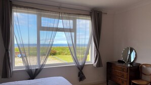 A bedroom with a bed, a dresser, a chair, and a large window with curtains.