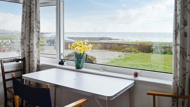 A room with a table and chairs near a window overlooking a beach.