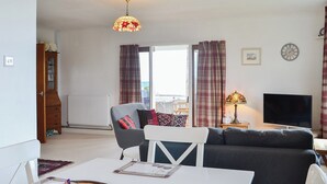 A living room with a sofa, a dining table with a bowl of fruit, a lamp, and a TV.