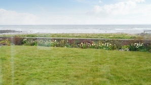 A grassy area with a view of the sea and a distant person walking.