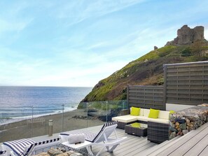 Terraço com área de estar ao ar livre, vista para uma praia e uma estrutura que lembra um castelo.