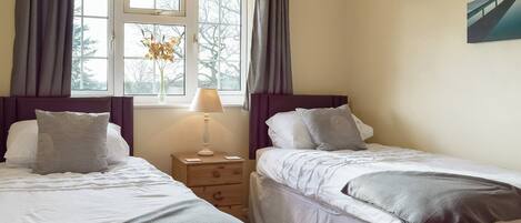 Een slaapkamer met twee bedden, een nachtkastje, een lamp en een raam met gordijnen.
