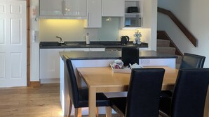 A modern kitchen with white cabinets, a wooden dining table, black chairs, and a staircase leading to another level.