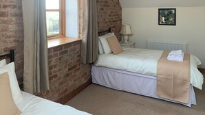 A bedroom with a brick wall, a window with curtains, a bed with white bedding, a bedside lamp, and a framed picture on the wall.