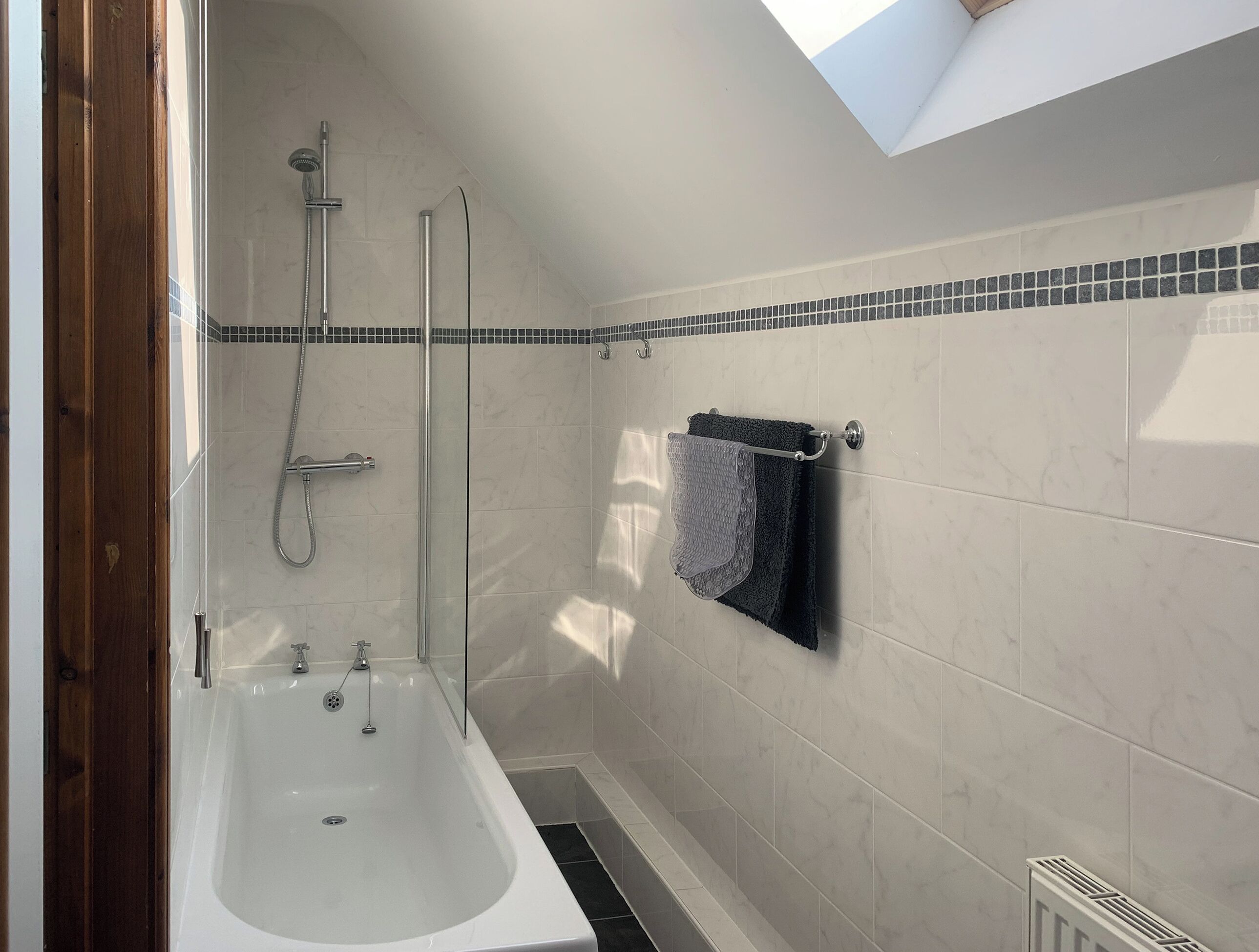 A modern bathroom with a bathtub, shower, and towel rack.