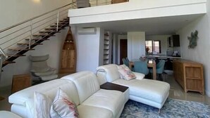 Un vaste espace de vie agrémenté d’un canapé blanc, d’un tapis à motifs et d’un escalier menant à un niveau supérieur.
