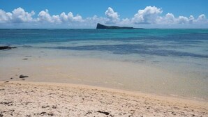 Une plage à l’eau turquoise et limpide, un rivage sablonneux et une île qui se dessine à l’horizon.