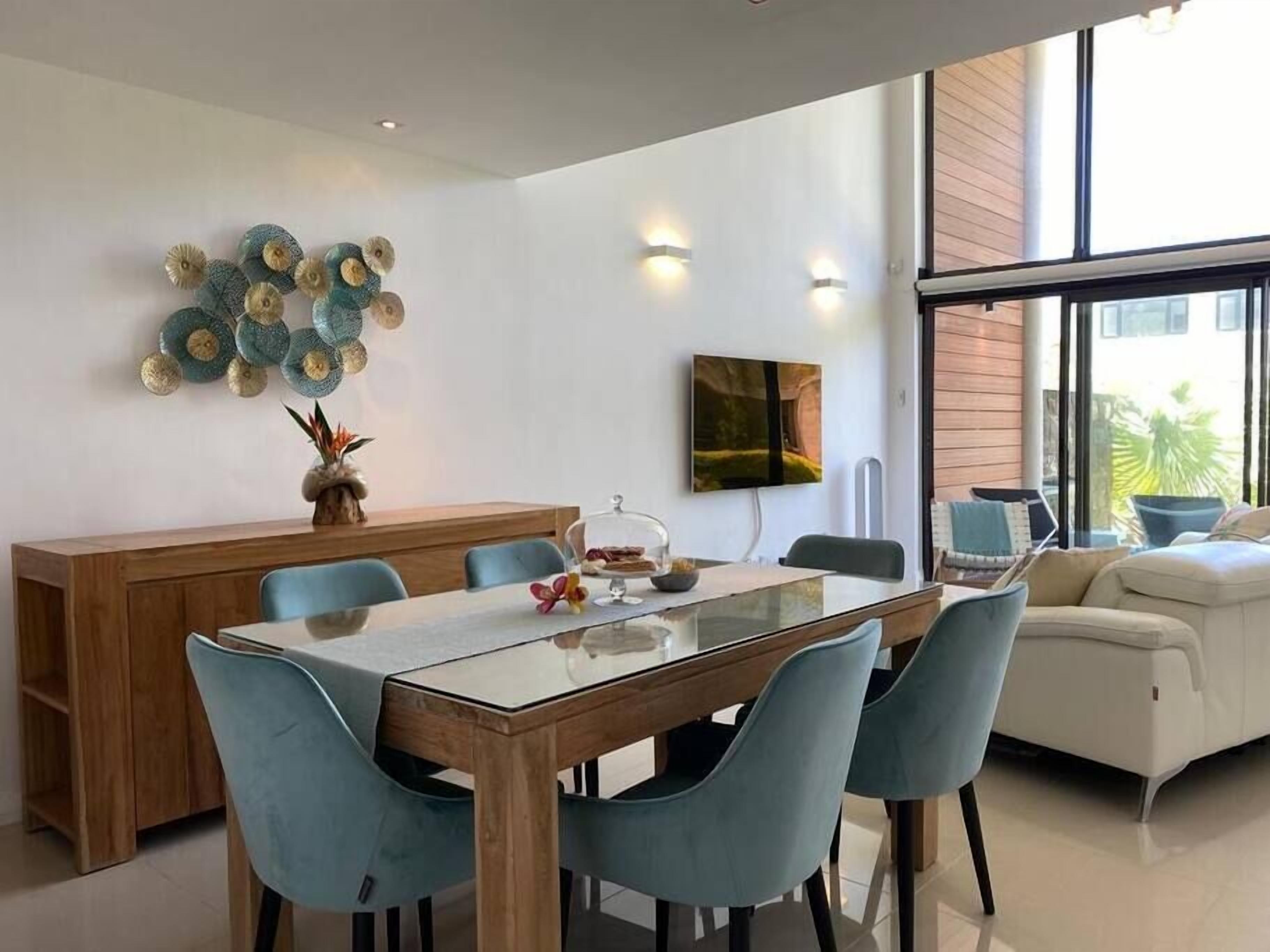Un espace repas moderne avec une table à plateau en verre, des chaises bleues et un buffet en bois.