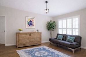 Una sala de estar con un aparador de madera, un sofá de cuero marrón, un tapete azul estampado, una lámpara colgante y una obra de arte enmarcada en la pared.