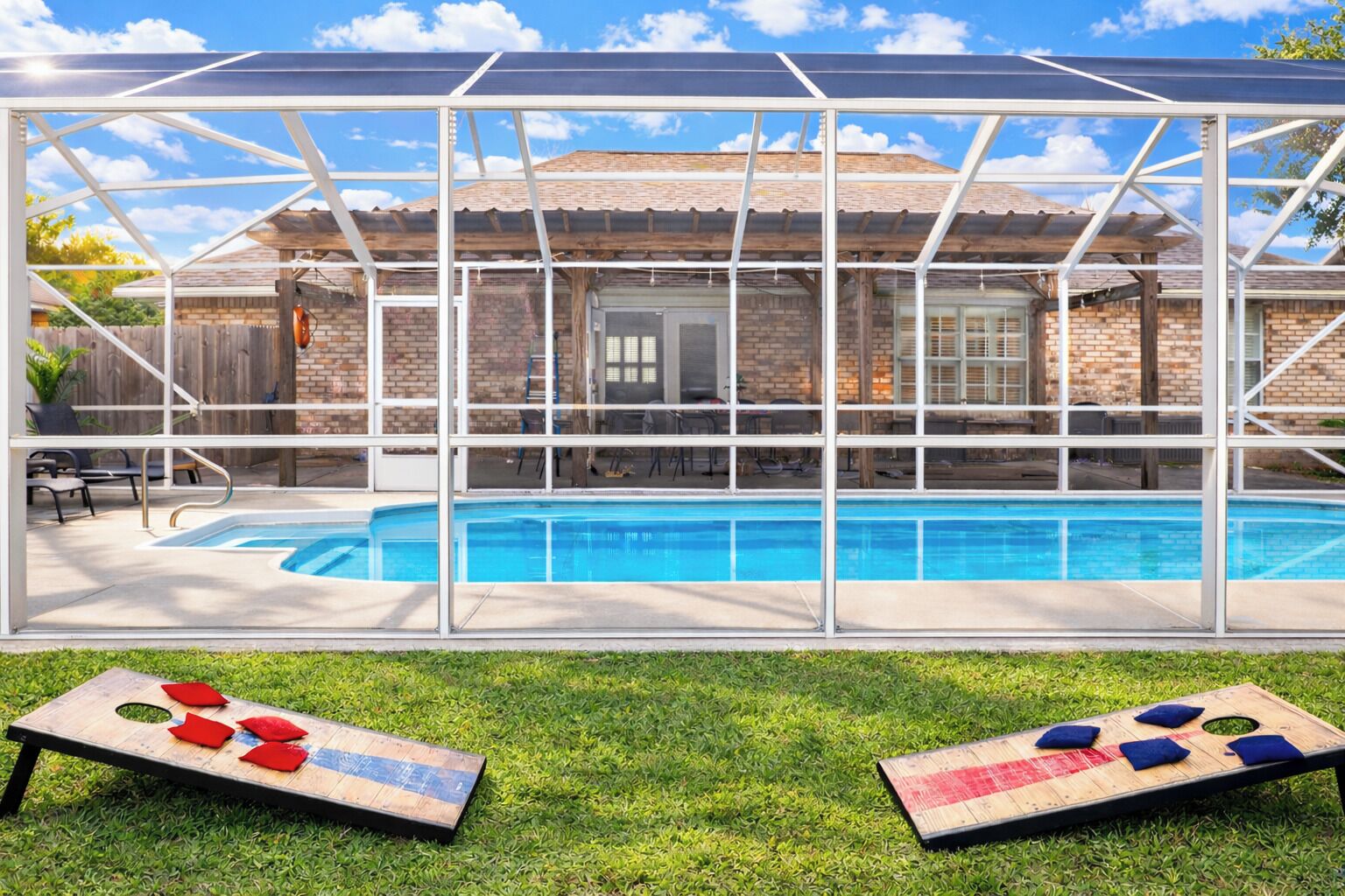 A pool with a glass enclosure, a grassy area with a game board, and a brick building in the background.