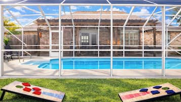 A pool with a glass enclosure, a grassy area with a game board, and a brick building in the background.
