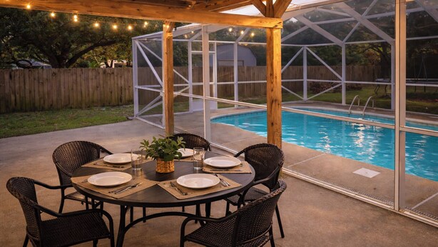 Um alpendre coberto com piscina, mesa de jantar, cadeiras e luzes de corda.