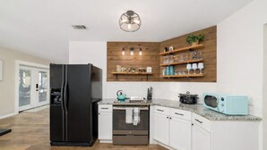 Uma cozinha moderna com geladeira preta, eletrodomésticos de aço inoxidável, prateleiras de madeira com copos e um micro-ondas verde água.