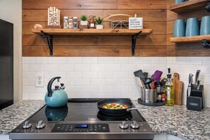 A kitchen with a stove, kettle, and various utensils.