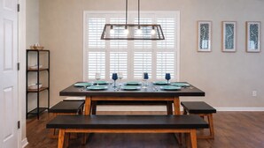 Uma área de refeições com uma mesa de madeira posta para quatro pessoas, um banco e um lustre.
