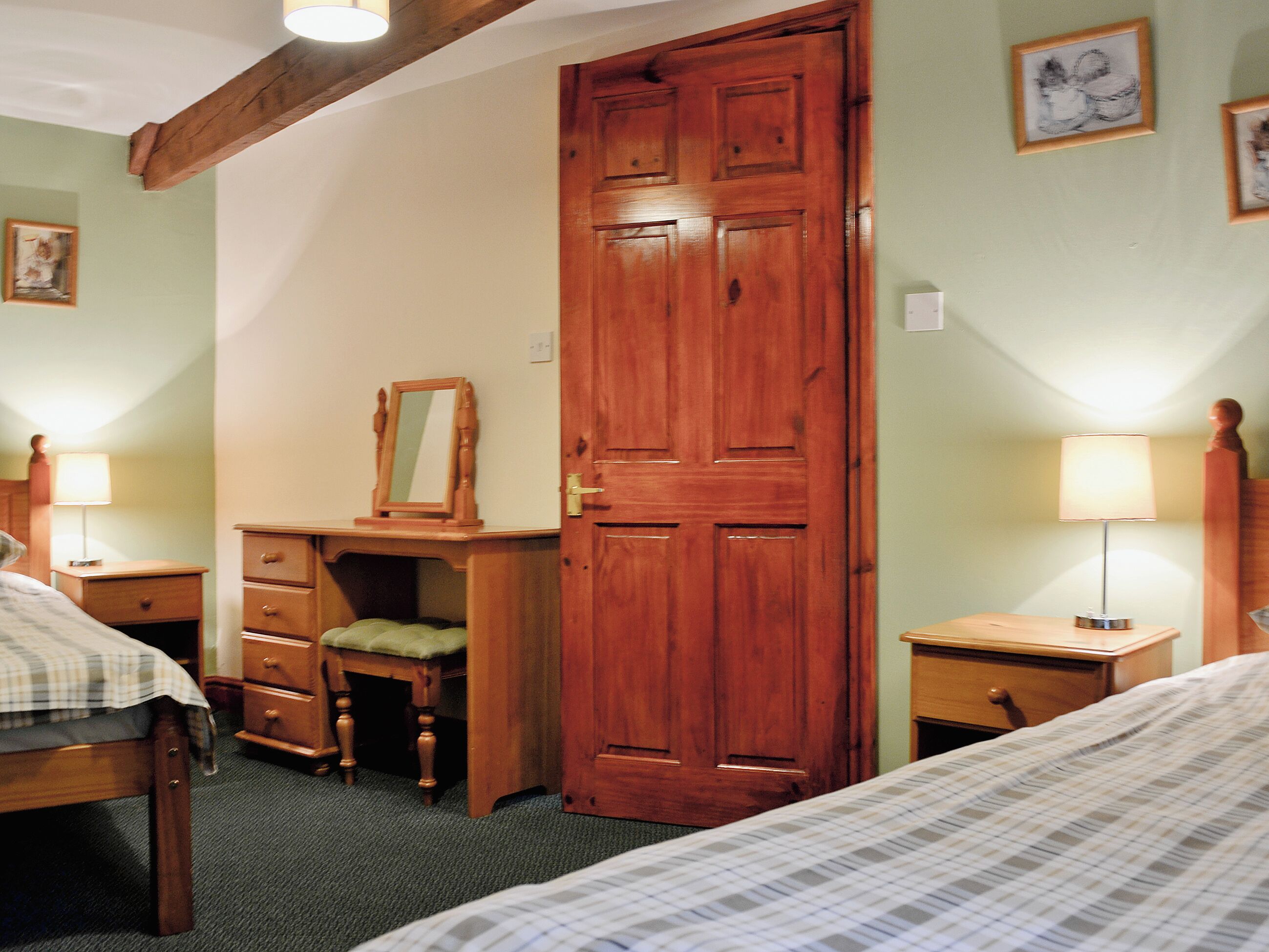 A bedroom with a wooden door, a dresser, a chair, two bedside tables with lamps, and a bed with a checkered bedspread.