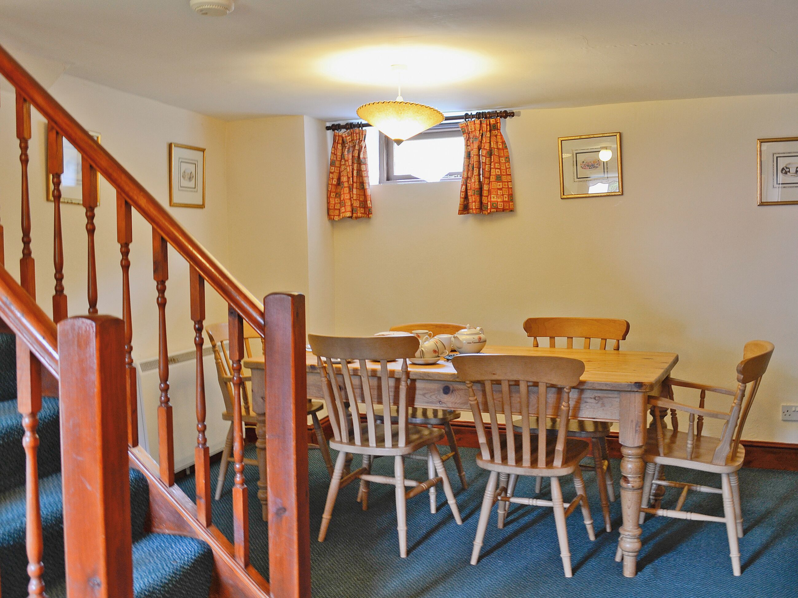 A dining area with a wooden table and chairs, a staircase, and a window with curtains.