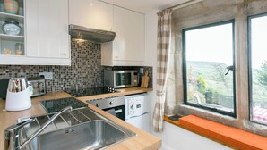 A modern kitchen with white cabinets, a stainless steel sink, a microwave, and a toaster. There is a window with a view of the countryside.