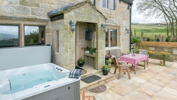 A stone building with a hot tub, outdoor seating, and potted plants.