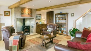 A cozy living room with leather sofas, a fireplace, a bookshelf, and a staircase leading to an upper level.