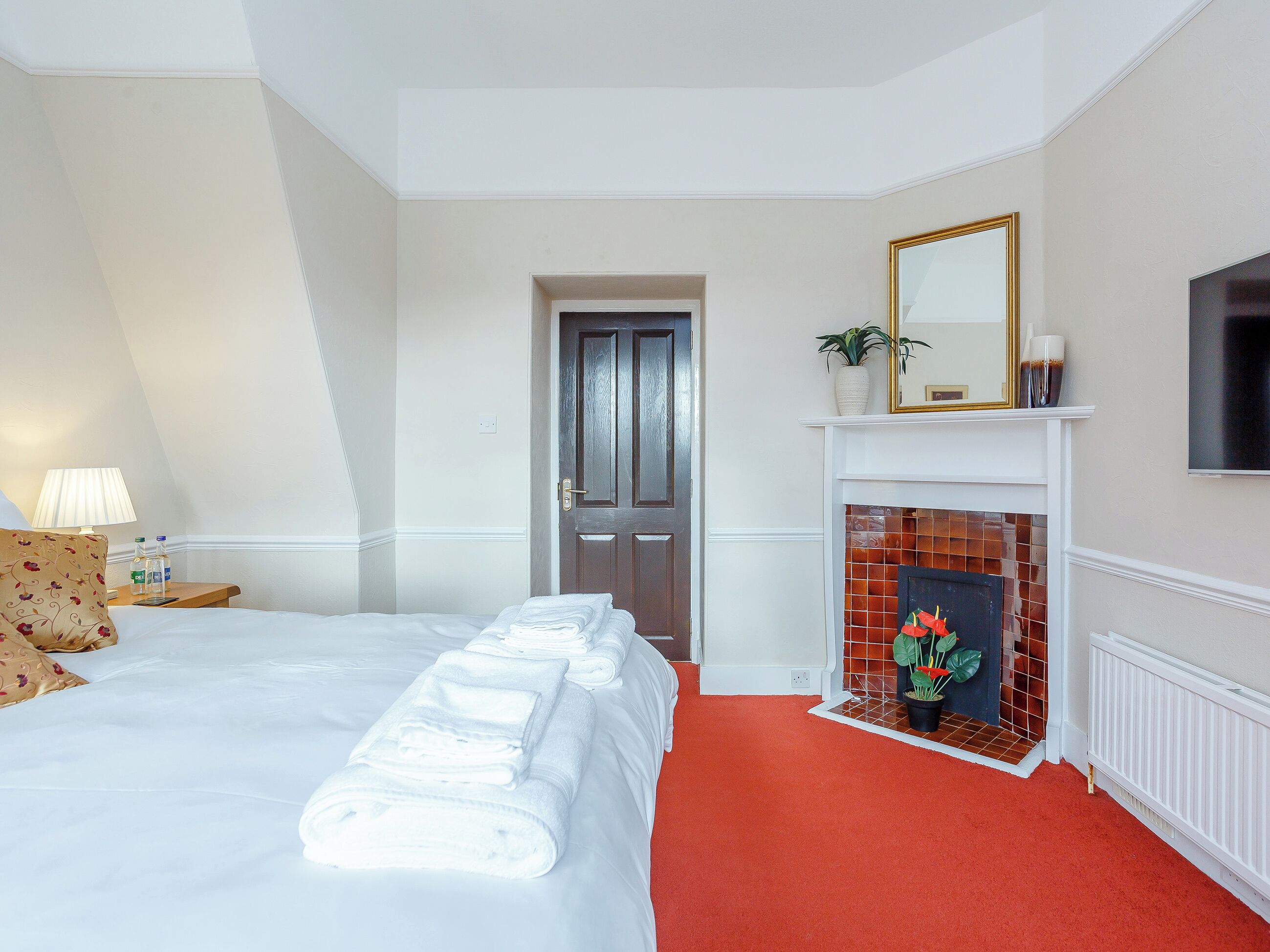 A hotel room with a neatly made bed, a fireplace, a TV, and a door leading to another room.