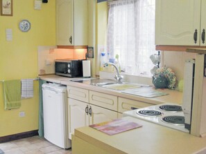Cozinha compacta com pia, fogão e micro-ondas. Há armários e uma janela com cortinas.