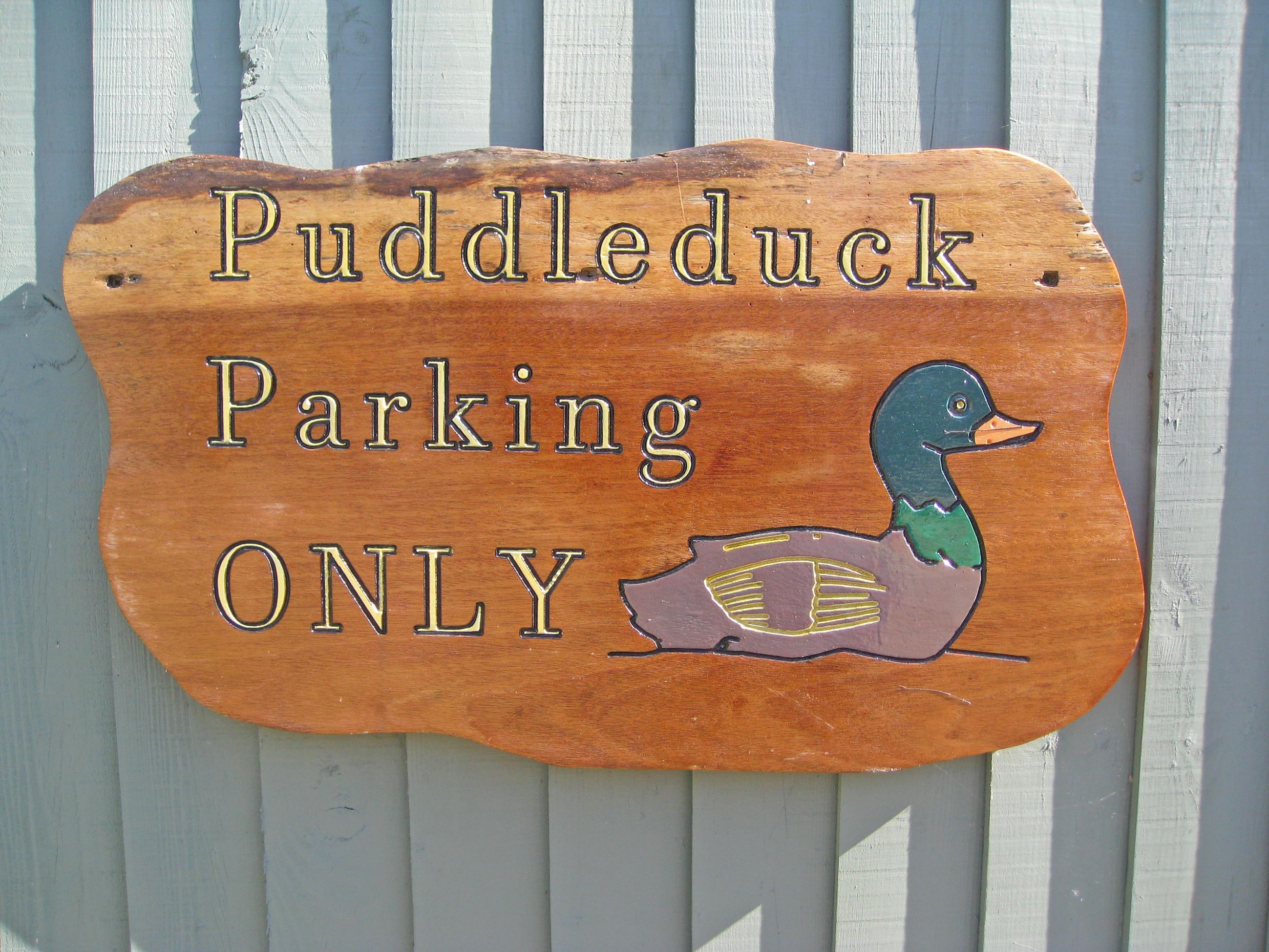 Un panneau en bois orné d’une illustration de canard et portant l’inscription : « Stationnement réservé aux véhicules de la marque Puddleduck ».