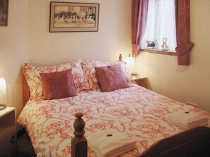 A bedroom with a bed, two nightstands, a bedside lamp, a framed picture on the wall, and a window with curtains.