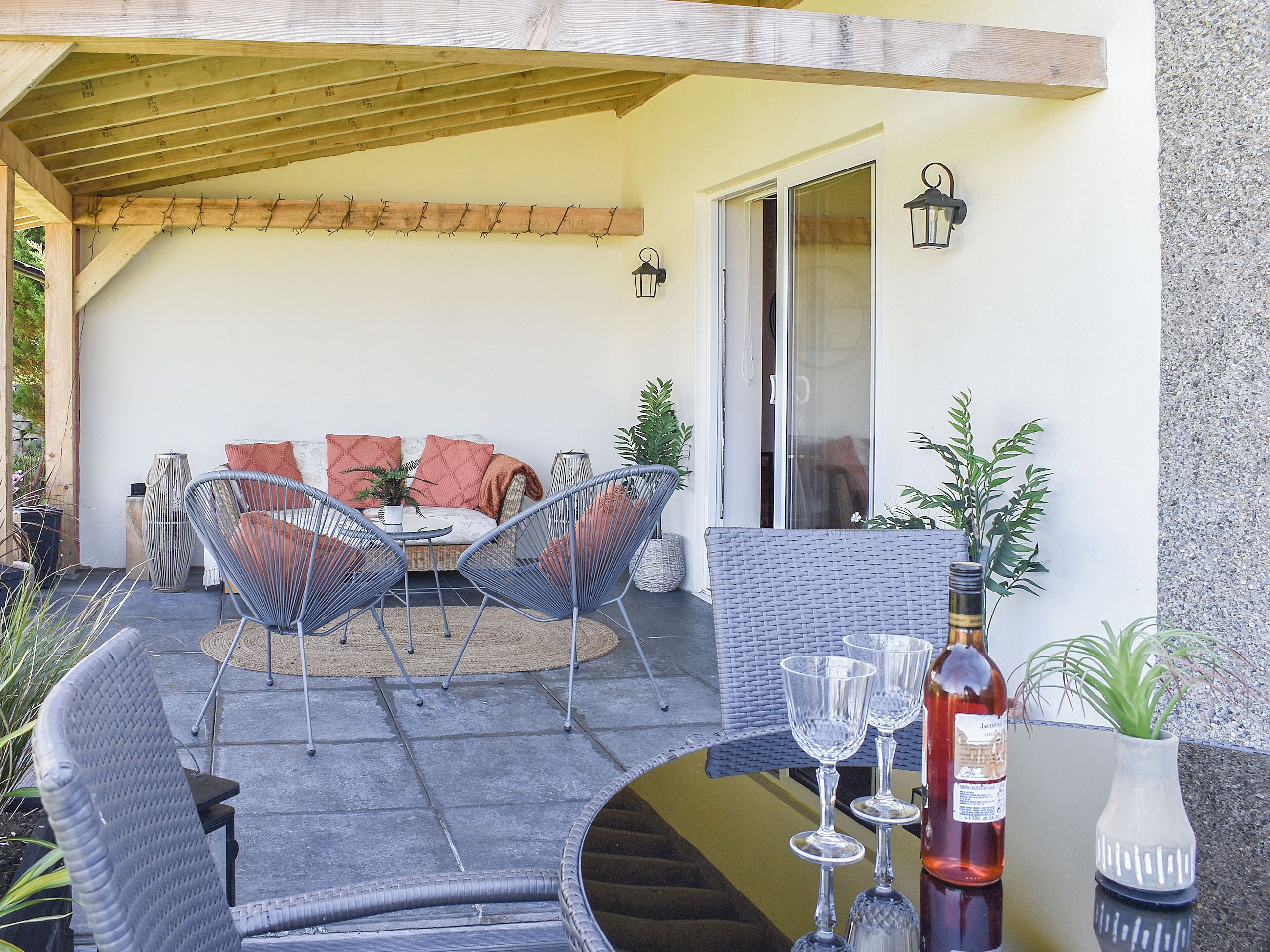 A covered patio with a sofa, two chairs, a table, and a bottle of wine.