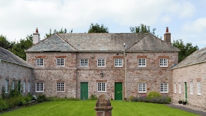 A stone building with multiple windows and a green door, surrounded by a well-maintained lawn.