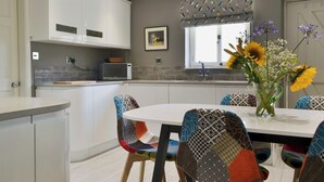 A modern kitchen with white cabinets, a microwave, and a dining area with colorful chairs and a vase of flowers.