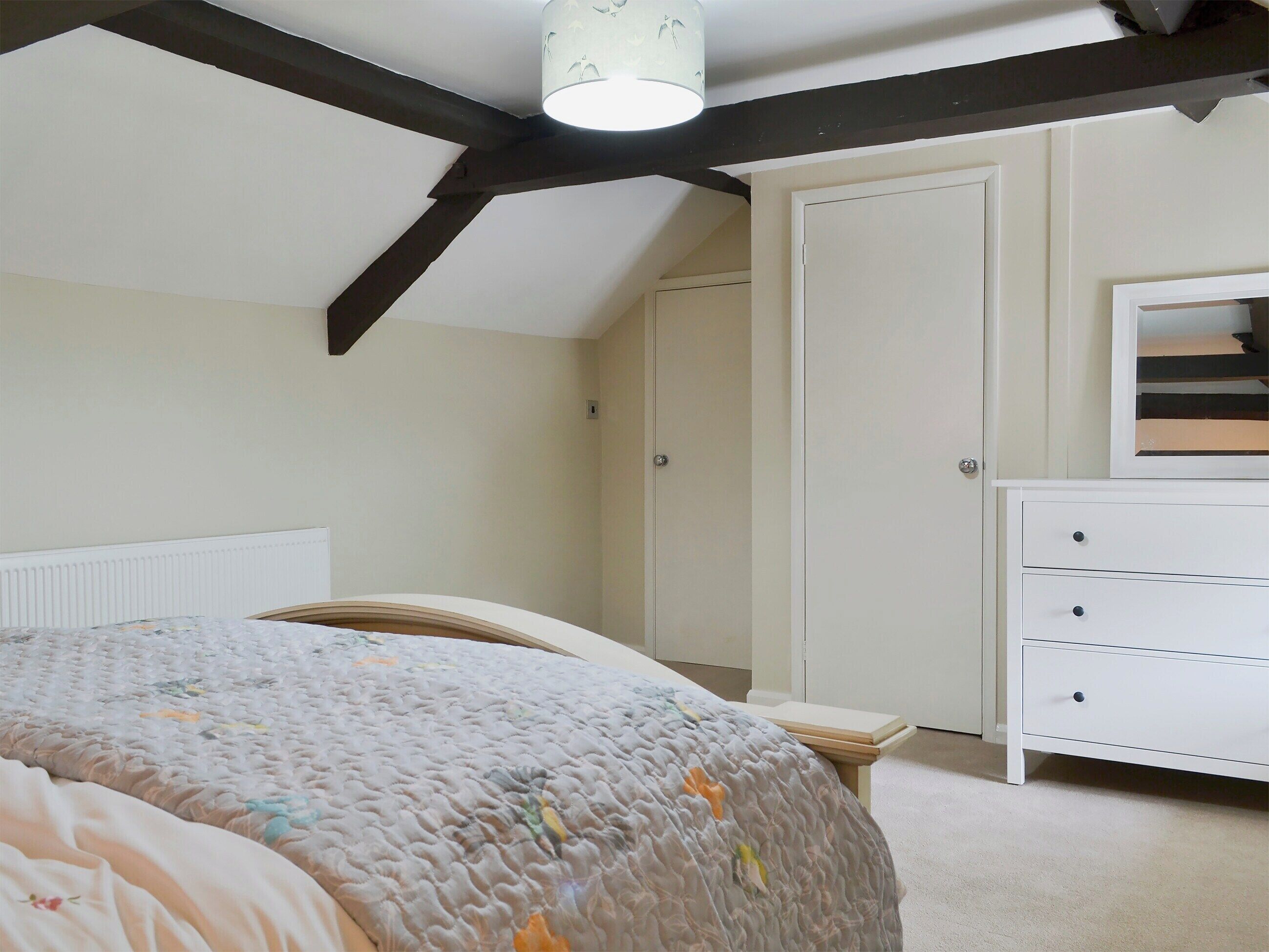 A bedroom with a bed, a dresser, a door, and a ceiling light.