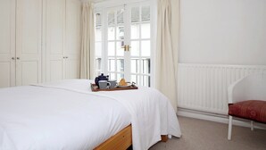 Une chambre avec un grand lit, une table de chevet en bois, une fenêtre avec des rideaux et un radiateur.