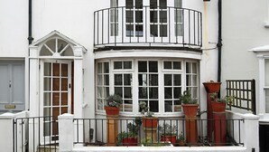 Un bâtiment blanc doté d’une baie vitrée, d’un balcon et de nombreuses plantes en pot.