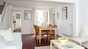 Un salon spacieux avec un coin repas, des meubles blancs et une vue dégagée sur l’extérieur grâce à une grande fenêtre.