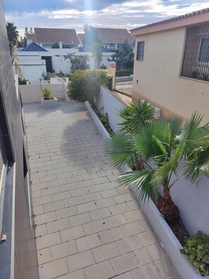 A paved patio area with potted plants and a white wall.