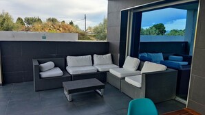 A modern outdoor seating area with a sofa and a table, a blue chair, and a view of greenery and a building in the background. - CASA DEL SOL, LUXURY AND RELAX BY THE SEA (Peñíscola)