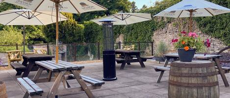 Een terras buiten met picknicktafels, parasols en een vat.