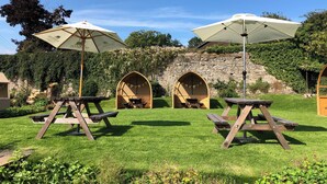 Un espace extérieur aménagé avec des tables de pique-nique et des parasols, entouré d’un mur de pierre et de verdure.
