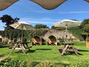 A patio area with picnic tables and umbrellas, surrounded by a stone wall and greenery. - The Old Kitchen -UK32062 (Burwarton, near Bridgnorth)