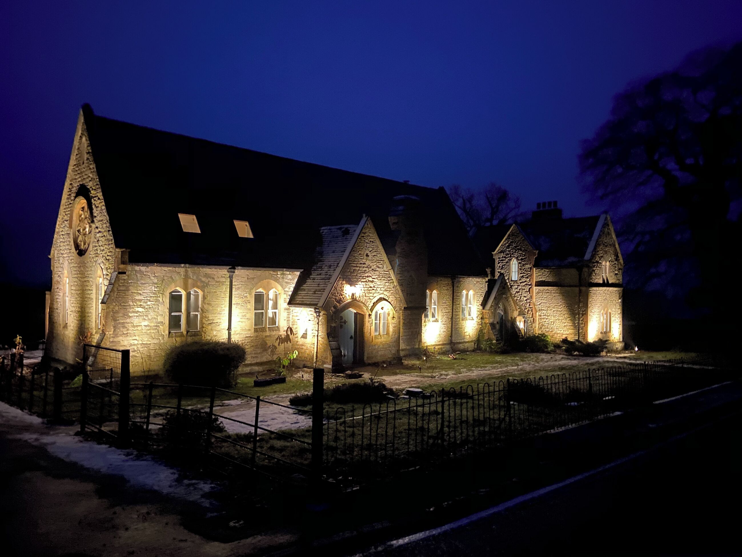 A stone building with arched windows and a large clock tower, illuminated at night.