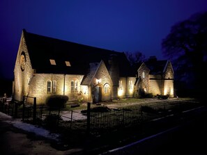 Een gebouw van steen met gebogen ramen en een grote klokkentoren, verlicht in de nacht.