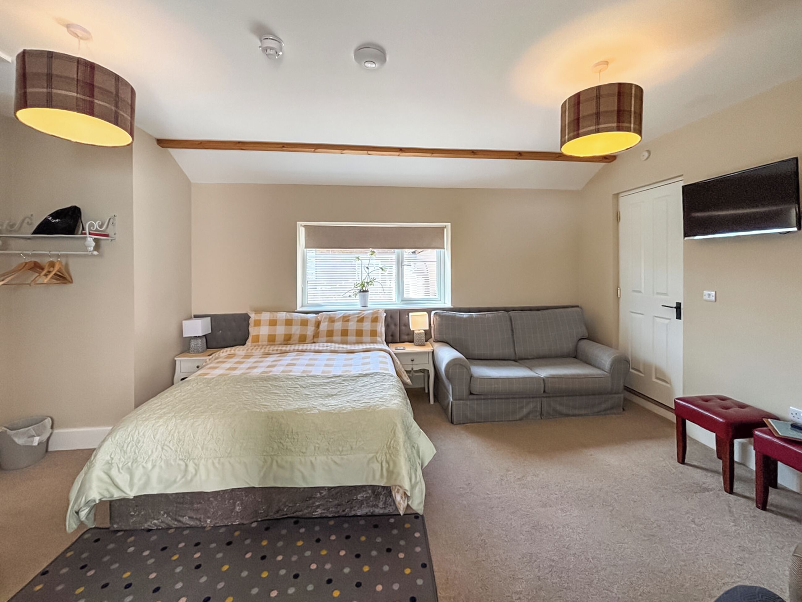 A bedroom with a bed, a sofa, a desk, a chair, a TV, and a window.