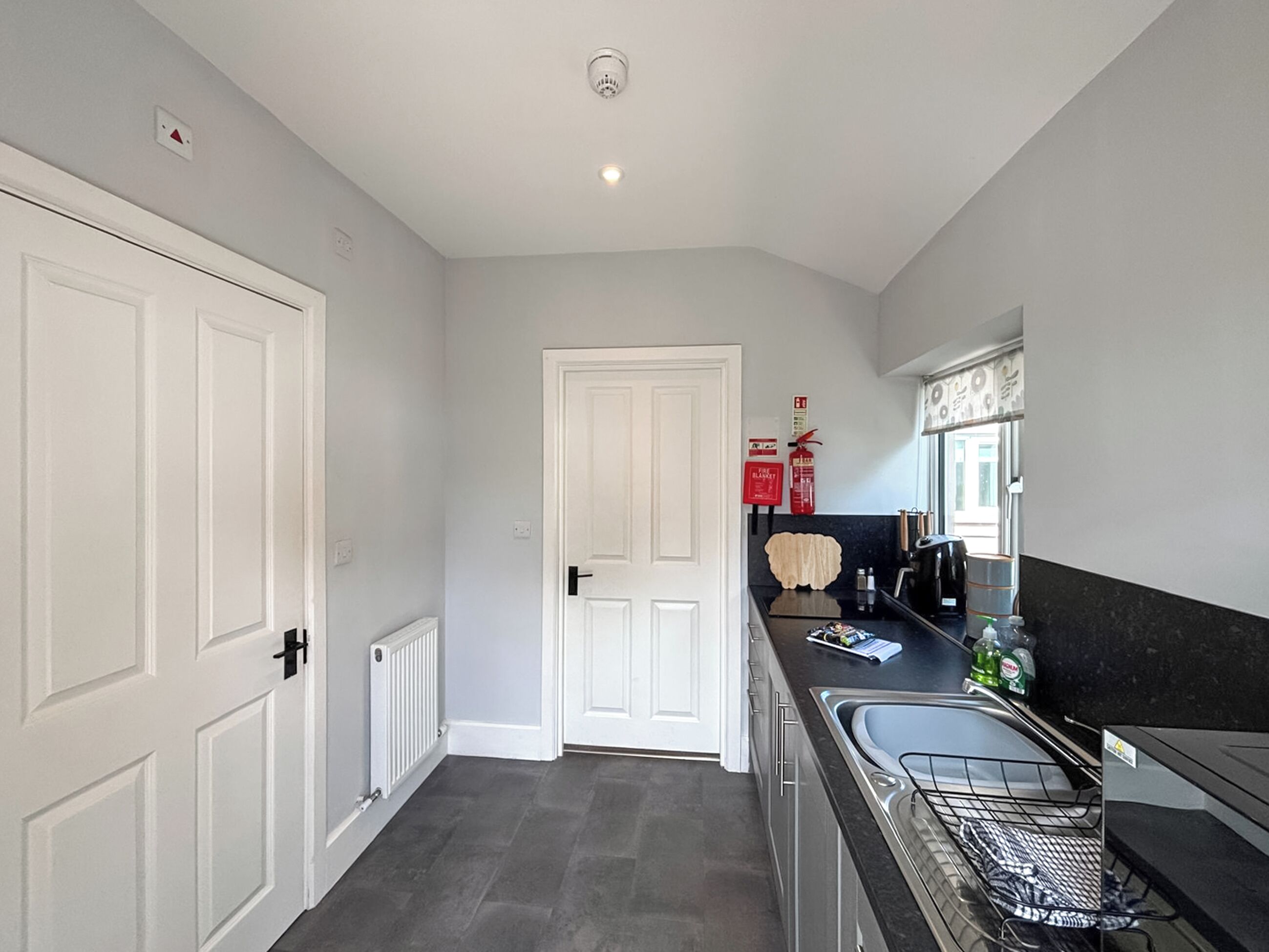 A narrow hallway with a white door, a radiator, and a kitchen area with a sink and countertop.