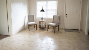 Una habitación con dos sillas, una mesita, una lámpara y una puerta.